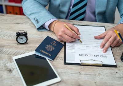 Close-up of male hands filling out visa documents at a table. On the table there is an American passport and an American flag