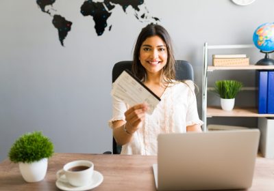 Excited female sales agent giving a client the plane tickets for their next holiday vacations while sitting at the travel office